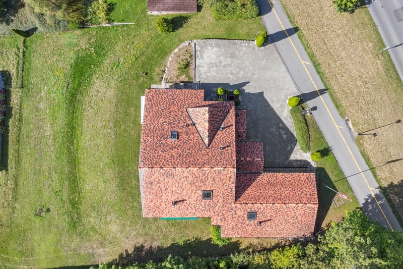 House with red tiles, triangular roof, driveway, elevated ground floor, garden, greenery