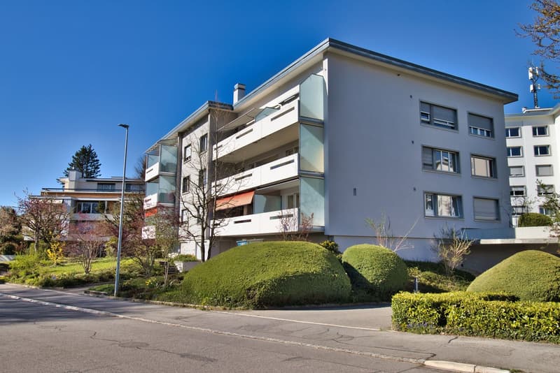 Modern white apartment building, multiple balconies, landscaped garden, street view