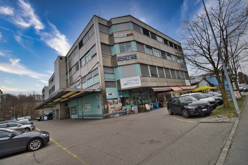 Office building with multiple floors, multiple cars parked in front, awnings over the entrance, sign reading 'airwartech'