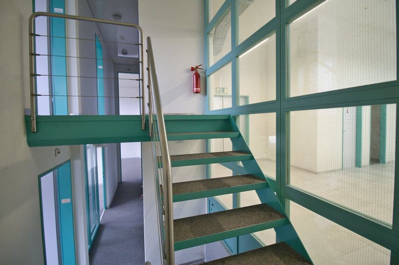 Green staircase with metal handrail, carpeted steps, glass walls, fire extinguisher mounted on wall