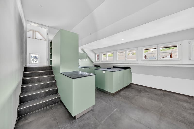 modern kitchen with green cabinets, black countertops, tiled floor, staircase, windows