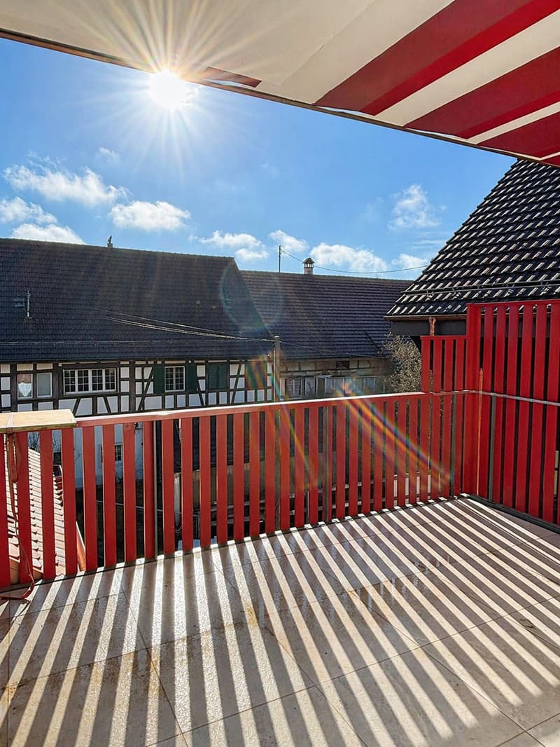 Balcony with red railings, tiled floor, view of the sky and buildings
