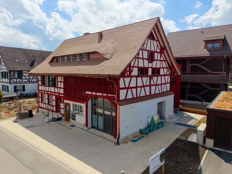 2 story house, red and white exterior, brown roof, large windows, glass doors, balcony, driveway