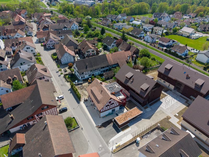 Aerial view of a neighborhood with several houses, some with brown roofs, a road, and a construction site.