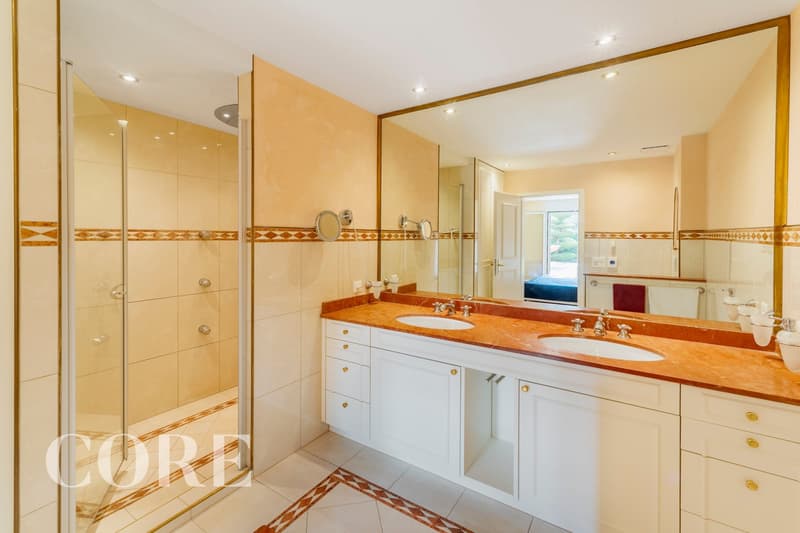 large mirror, double sink, shower, white cabinets, marble countertop, tiled floor