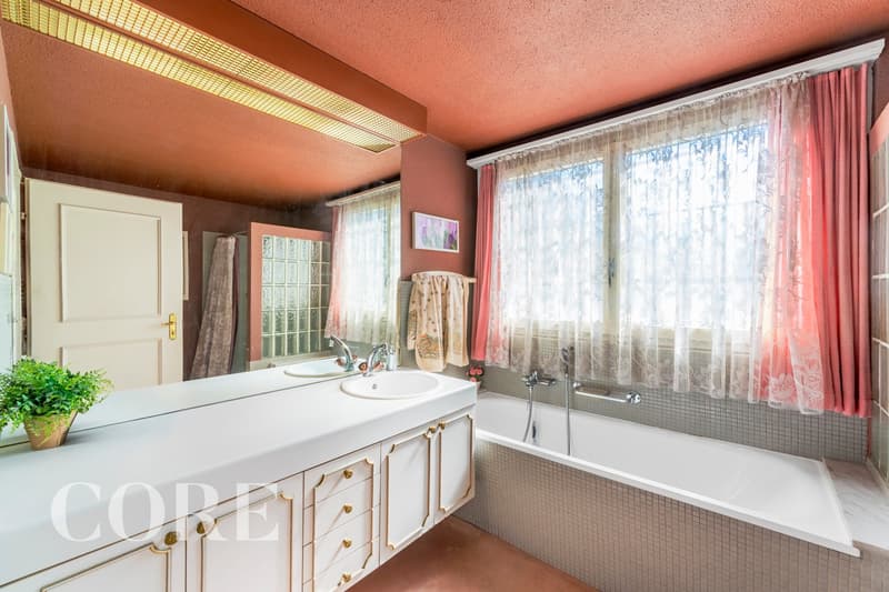 Bathroom with a bathtub, double sink, mirror, and a window with curtains.