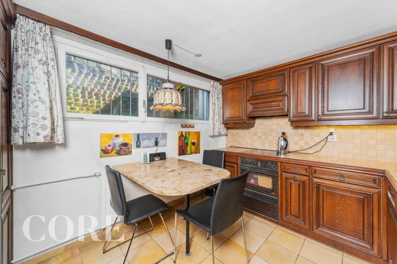 kitchen with wooden cabinets, tiled floor, dining table with 2 chairs, window with curtains, built-in oven, kettle, power outlet