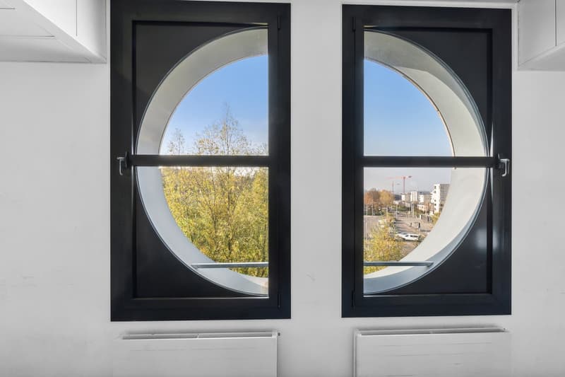 Two large arched windows with black frames overlooking a view of trees and buildings outside