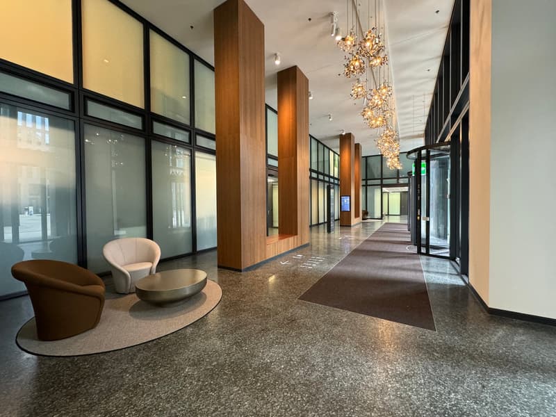 lobby area with modern design, wooden benches, glass walls, chandeliers, and a glass door