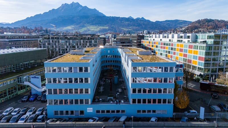 Office building, blue exterior, green roof, multiple floors, parking lot, city skyline