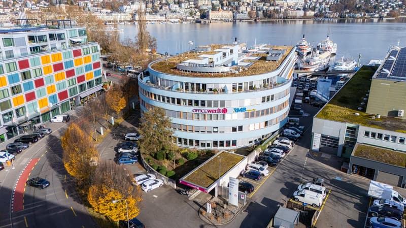 Modern office building with raised ground floor, green roofs, and surrounded by parking lots and boats