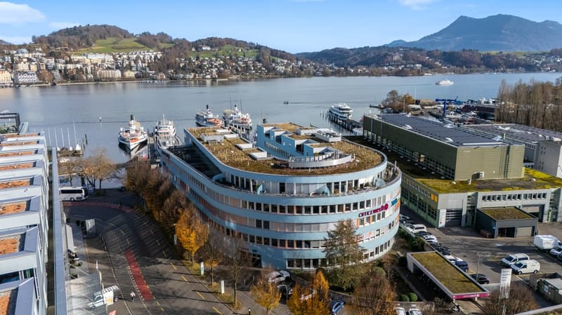 modern building, multiple floors, green roof, surrounded by trees, parking lot, boats docked