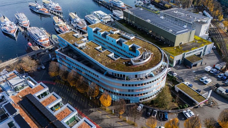 curved blue building, green rooftop, nearby dock with ships, parking lots, multiple buildings, multiple cars