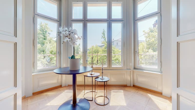 white walls, wooden floor, large arched windows, decorative table with plant and candle holder