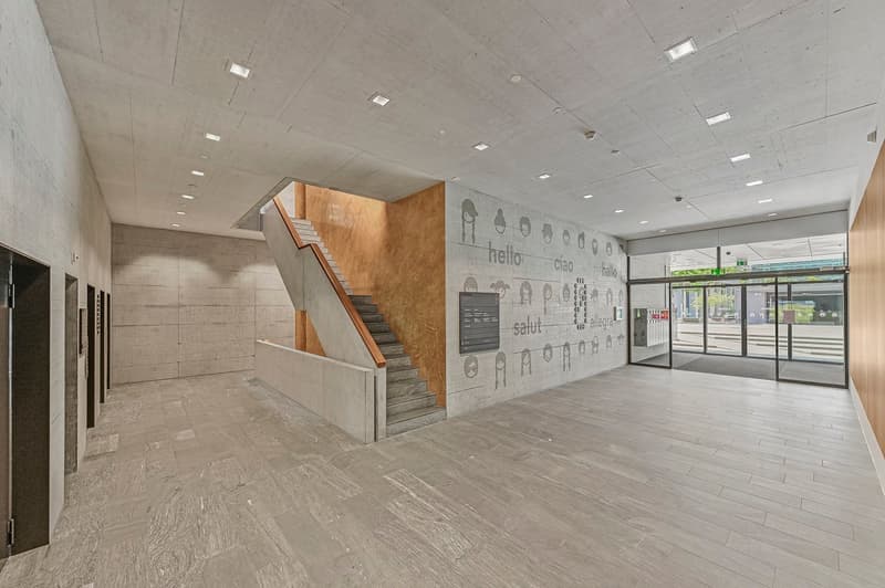 Open space, large tiles, wooden stairs, grey walls, bright lights