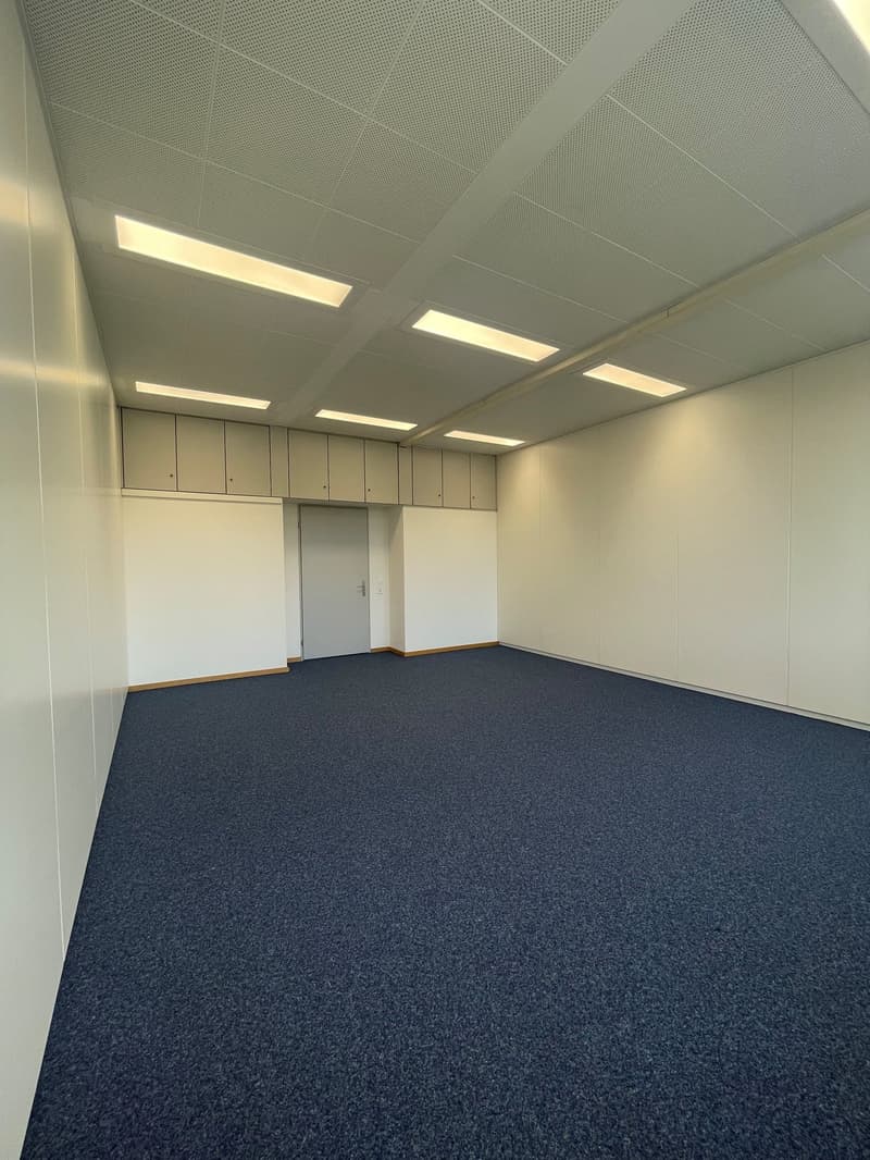 empty room, dark blue carpet, white walls, ceiling lights, cabinets on one side, door at end of room