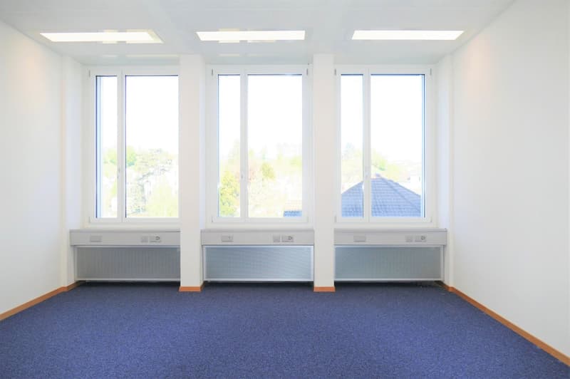 A room with 3 windows with wooden frames, blue carpet, ceiling lights, air vents in the window sills