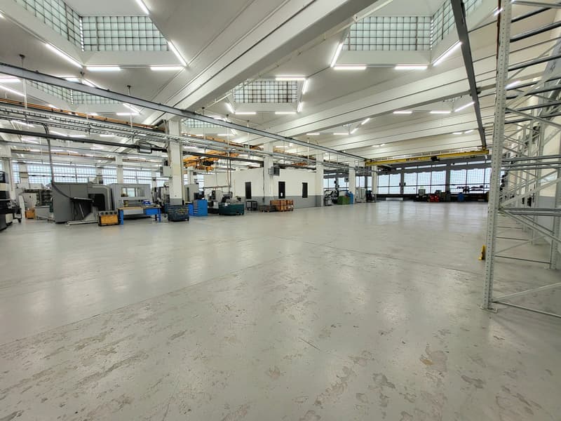Large industrial warehouse space with high ceilings, concrete floors, and various machinery and equipment visible. The space appears to be used for manufacturing or storage purposes.