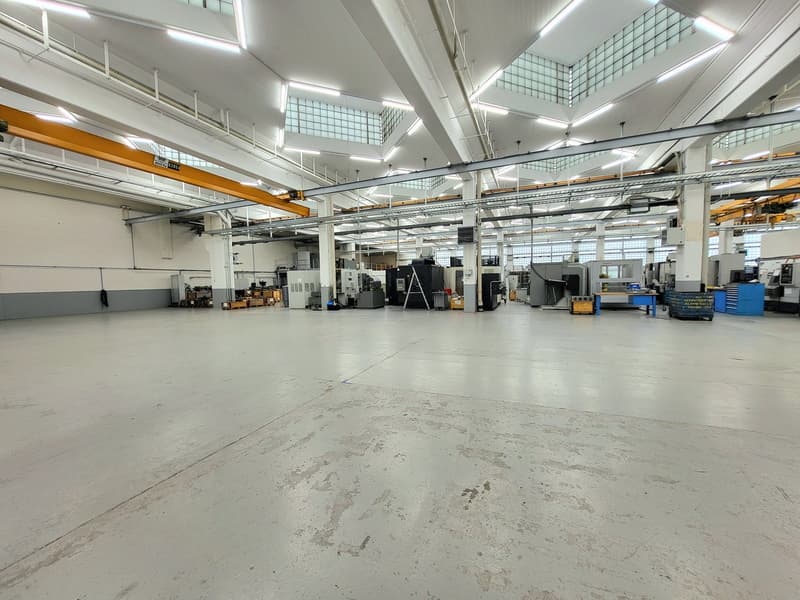 Large industrial warehouse space with high ceilings, overhead cranes, and various machinery and equipment visible.