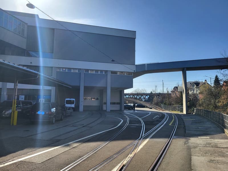 a large building with glass windows, cars parked in front, tramway tracks