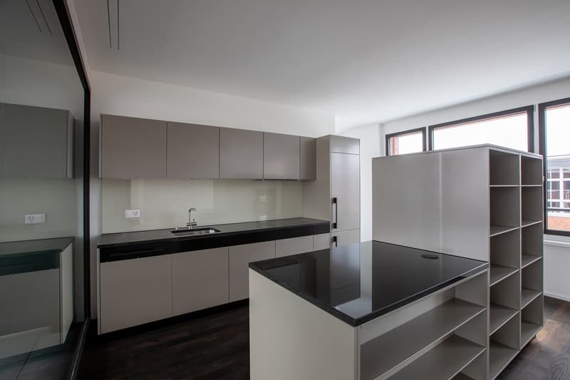 Modern kitchen with gray cabinets, black countertops, stainless steel sink, large windows, wooden floor