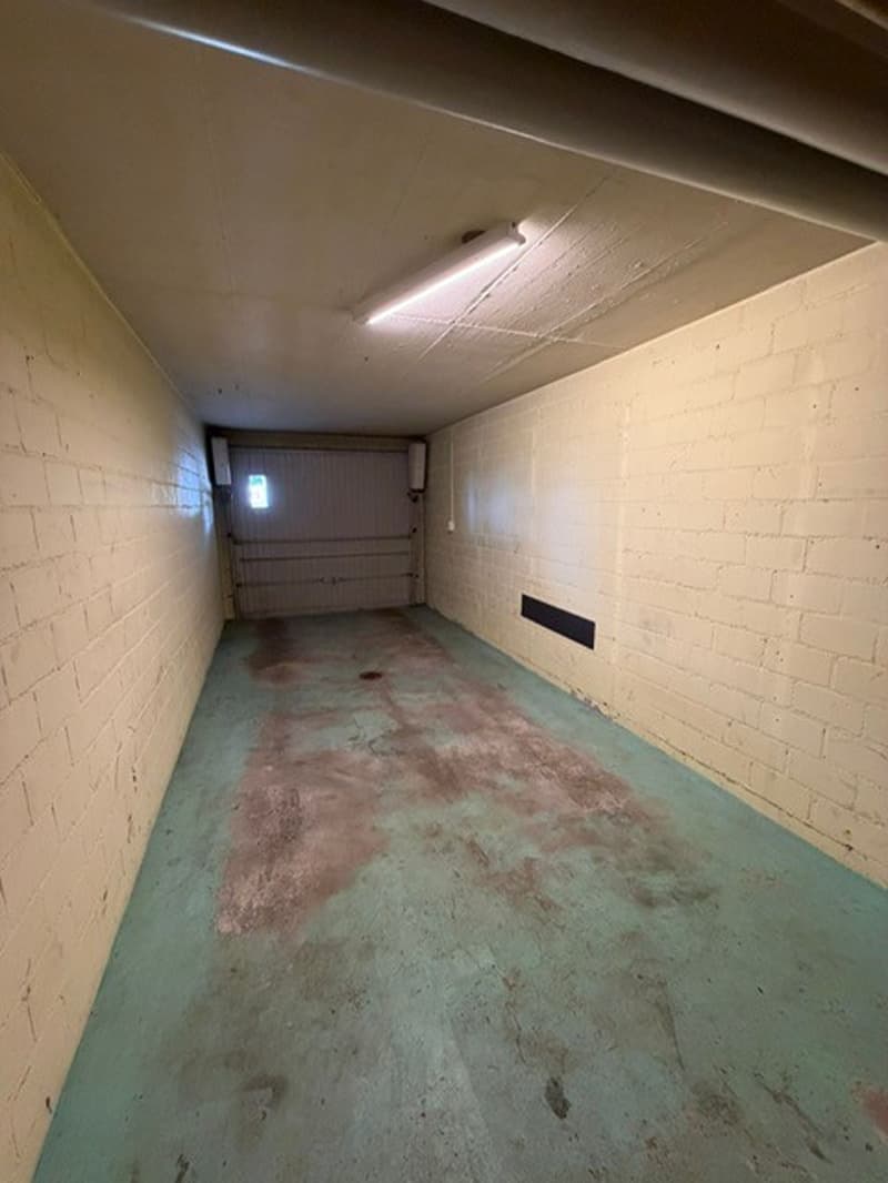 Empty garage with white brick walls, a ceiling light, and a concrete floor