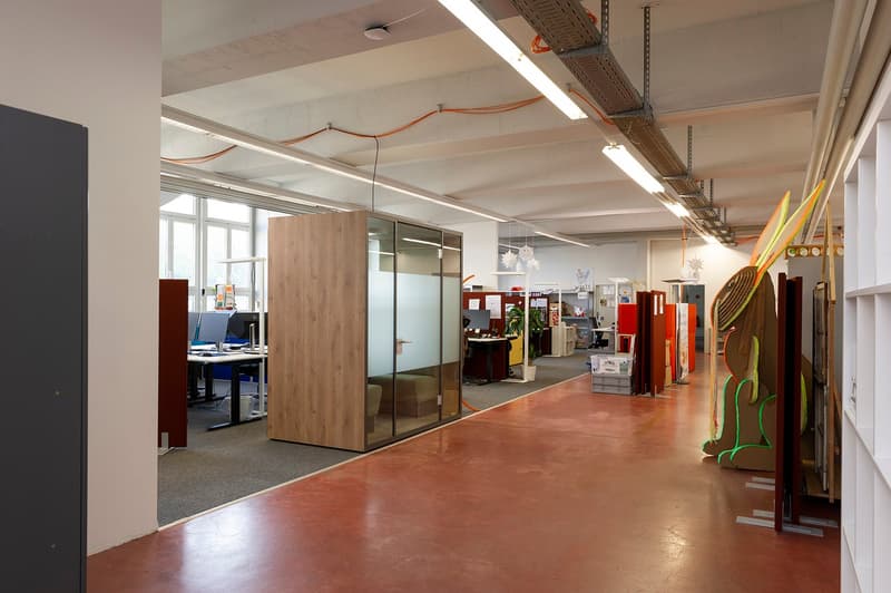 Open office space with concrete floors, exposed ceiling, glass partitions, desks, and various office equipment and decor