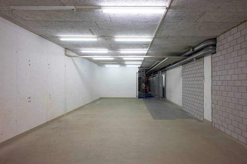 Empty basement parking room with concrete walls, ceiling pipes, and lights