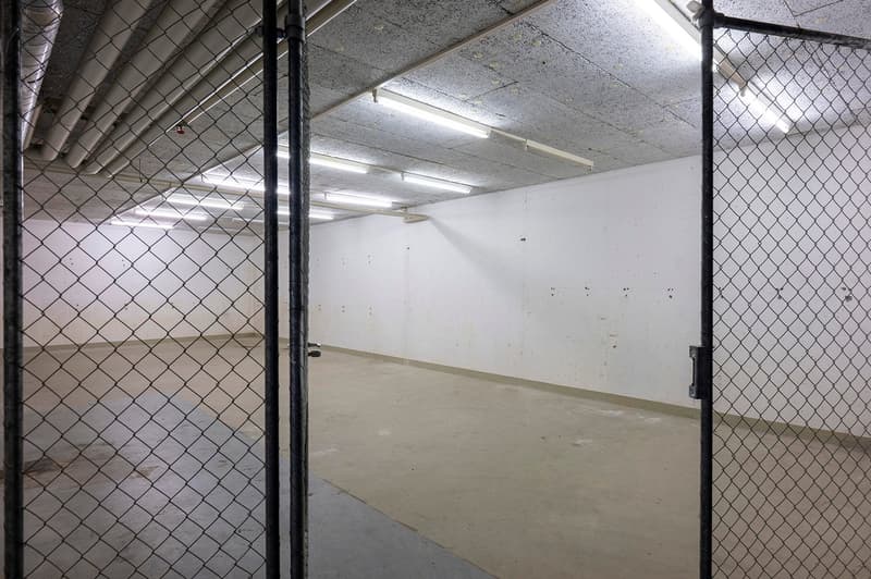 Empty garage with concrete floor, white walls, and chain-link fence