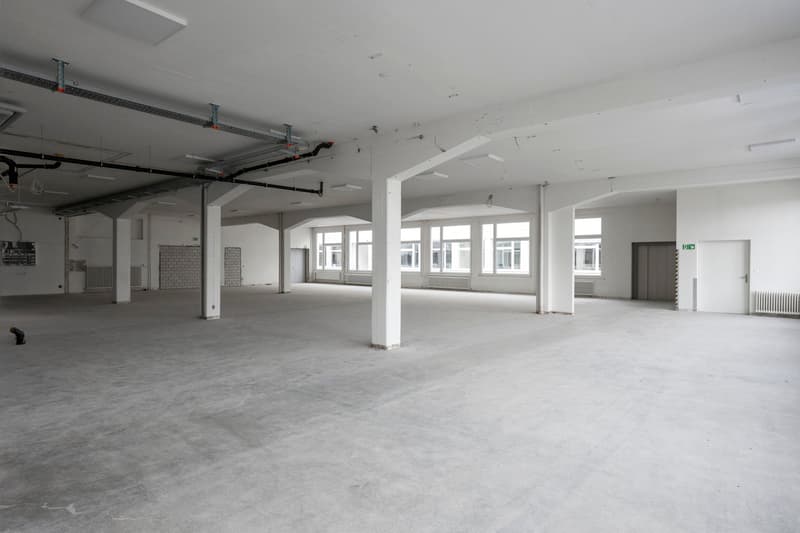 spacious, high ceiling, concrete floor, several white pillars, windows, ventilation shafts, empty
