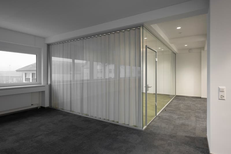 Glass wall with white curtains, white ceiling, gray carpet, a white radiator, a window