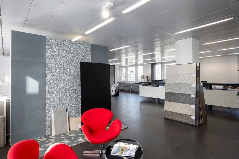 office room, modern interior design, grey and black walls, dark flooring, red chairs, illuminated ceiling lights, black and white desk, magazine table