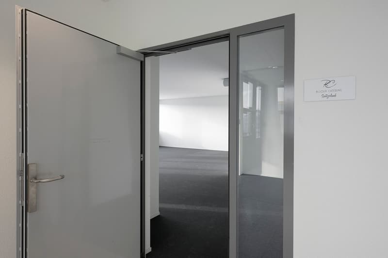 An open doorway leading to a wide, well-lit hallway, with a glass door on the right side.