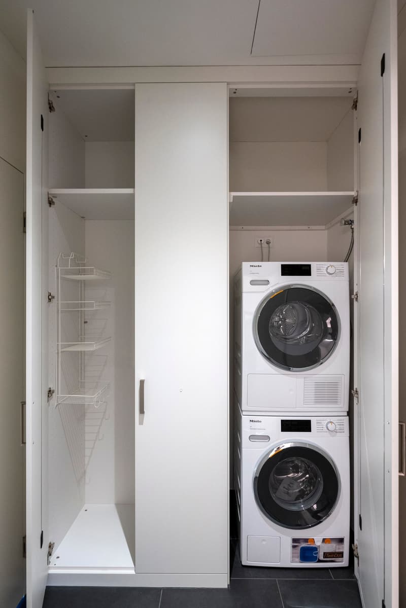 Laundry room with white cabinets, shelving unit, and Miele washing machine and dryer