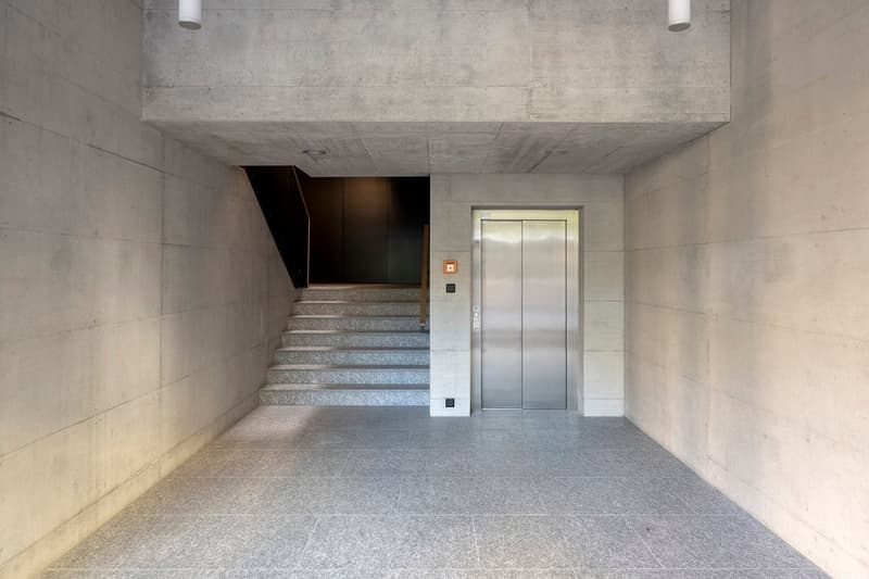 Concrete walls, gray tiled floor, elevator, stairs