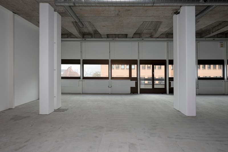 Open space with white walls and columns, large windows, concrete floor, exposed ceiling beams