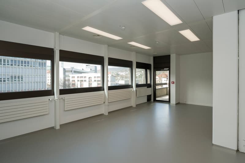spacious room with gray flooring, white walls, multiple large windows, and panel heaters