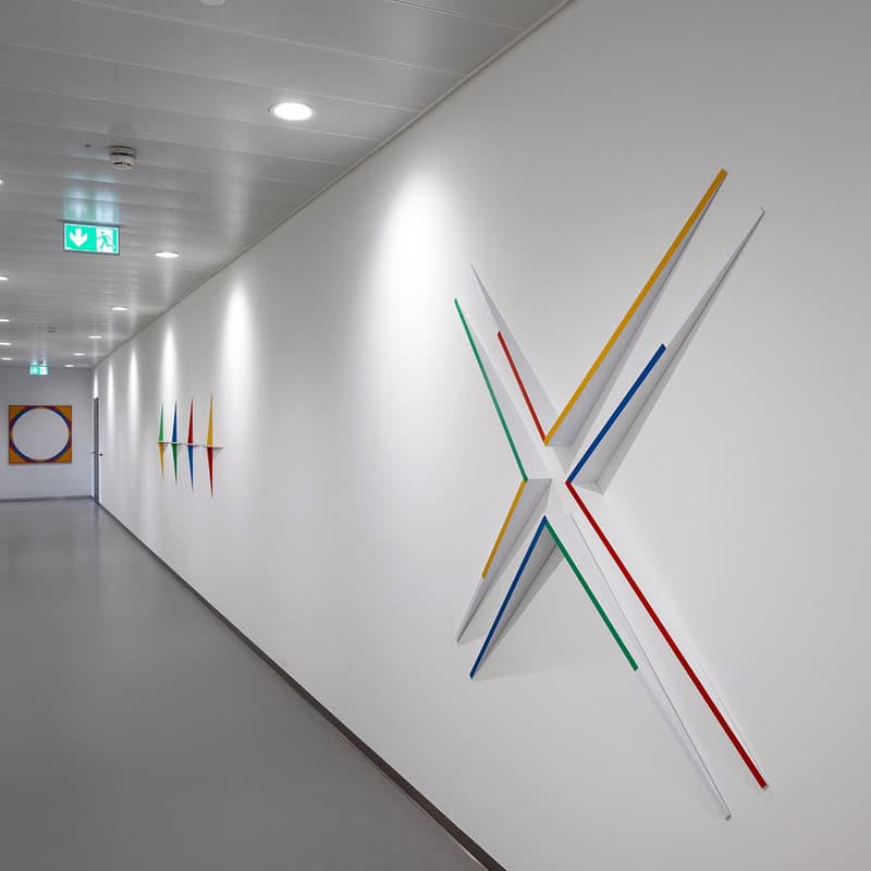 Empty corridor with a white wall and multiple colorful artworks attached to it