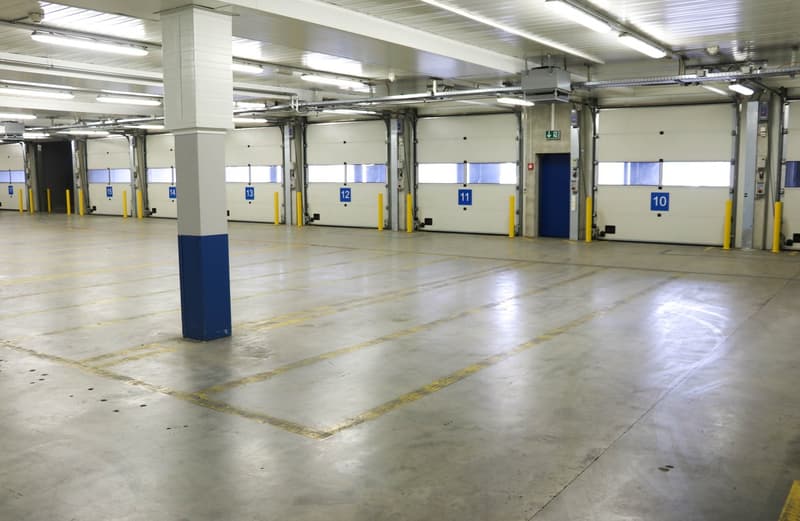 Empty parking lot with numbered parking spaces, white and blue pillars, yellow markings, and overhead lighting.