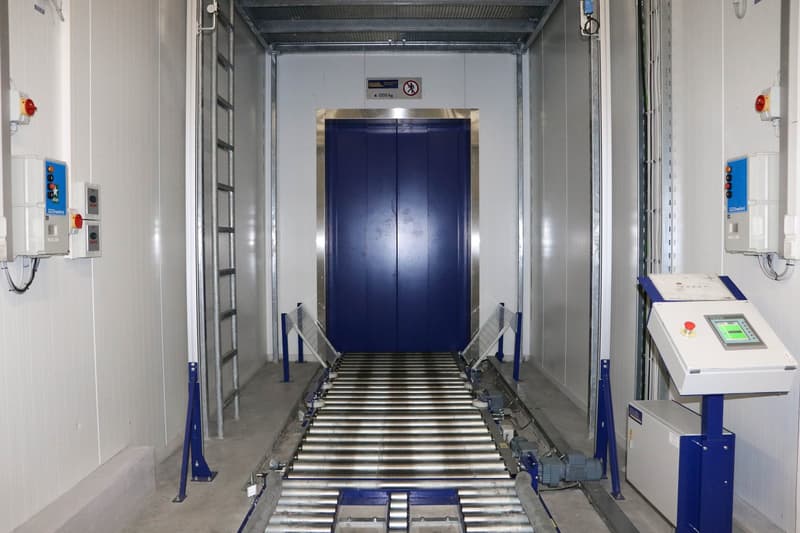 Industrial facility with a large blue door, a conveyor belt, and control panels on the wall.