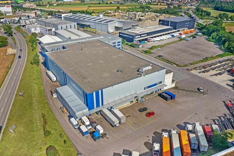 Industrial building with multiple sections, large parking lot, multiple trucks parked, road leading to the building