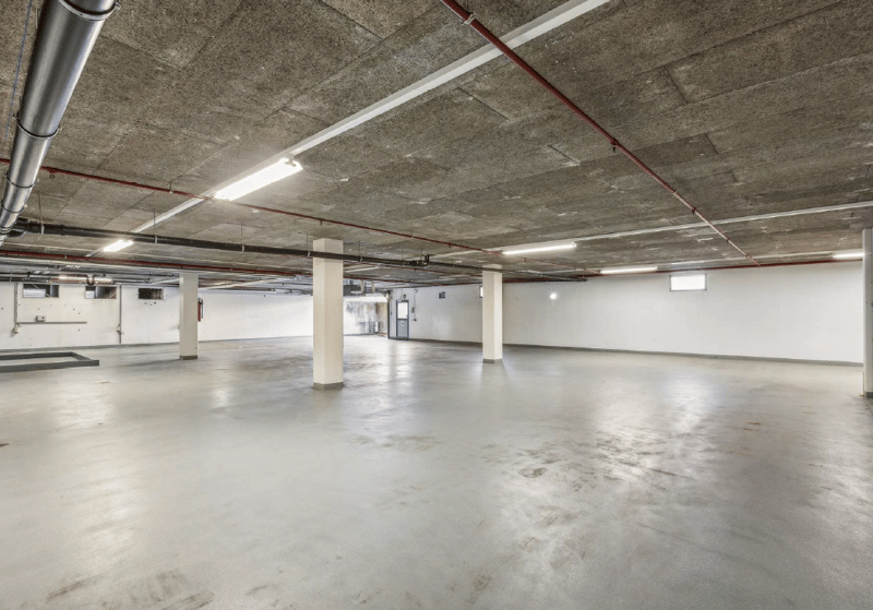 Empty parking lot with concrete floor, white walls, and metal beams with pipes