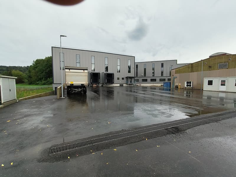 Industrial building with large windows, two large doors, a truck parked in front, and a paved parking lot.