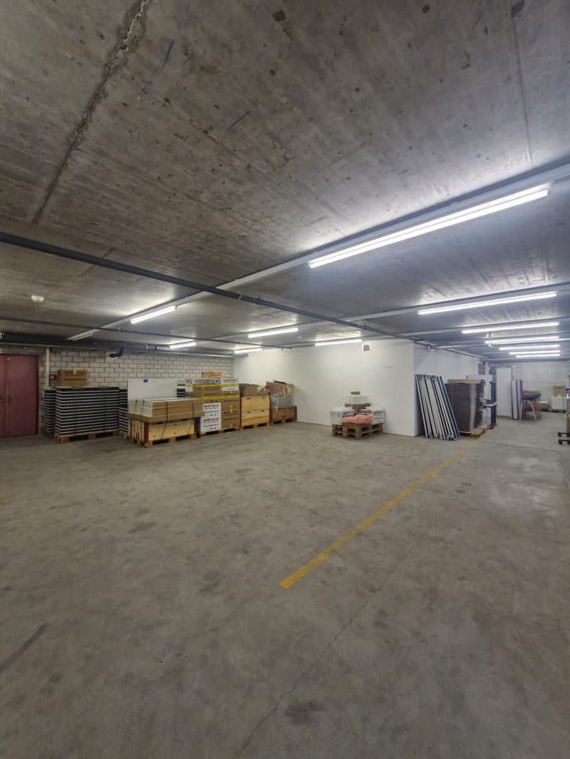 Large concrete room, ceiling lights, large yellow line, storage boxes, a door at the far end.