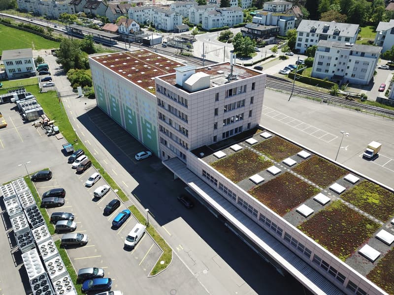 A commercial building with a green roof, adjacent to a parking lot, featuring multiple vehicles and street lights.