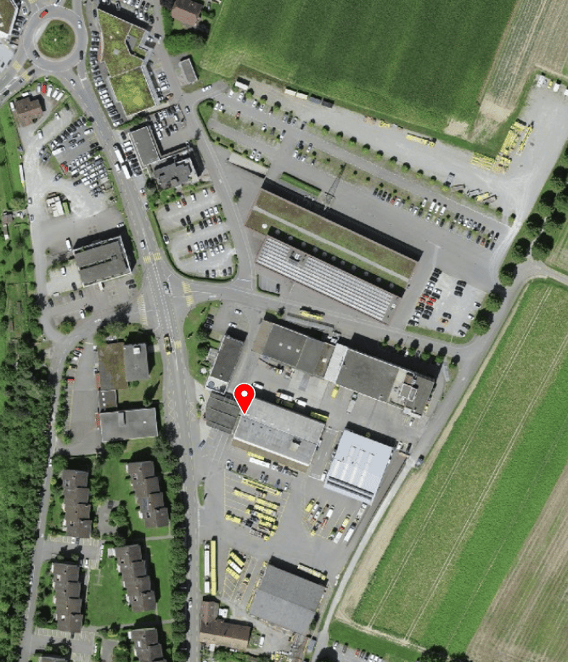 a complex of buildings including residential buildings, industrial buildings, and a parking lot with several rows of vehicles