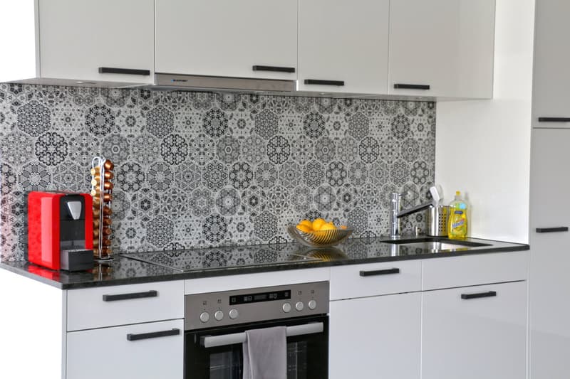 Modern white kitchen, black countertops, gas stove, oven, tiled backsplash, sink, faucet, bowl of lemons, dishwashing liquid, white cupboards