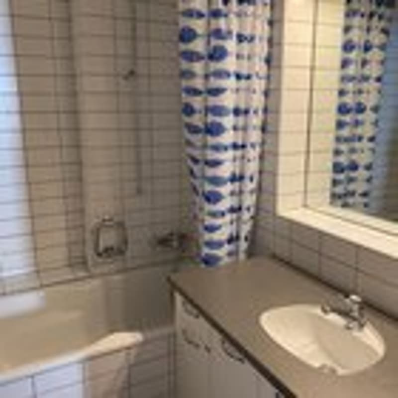 Bathroom with a bathtub, sink, mirror, and tiled walls.