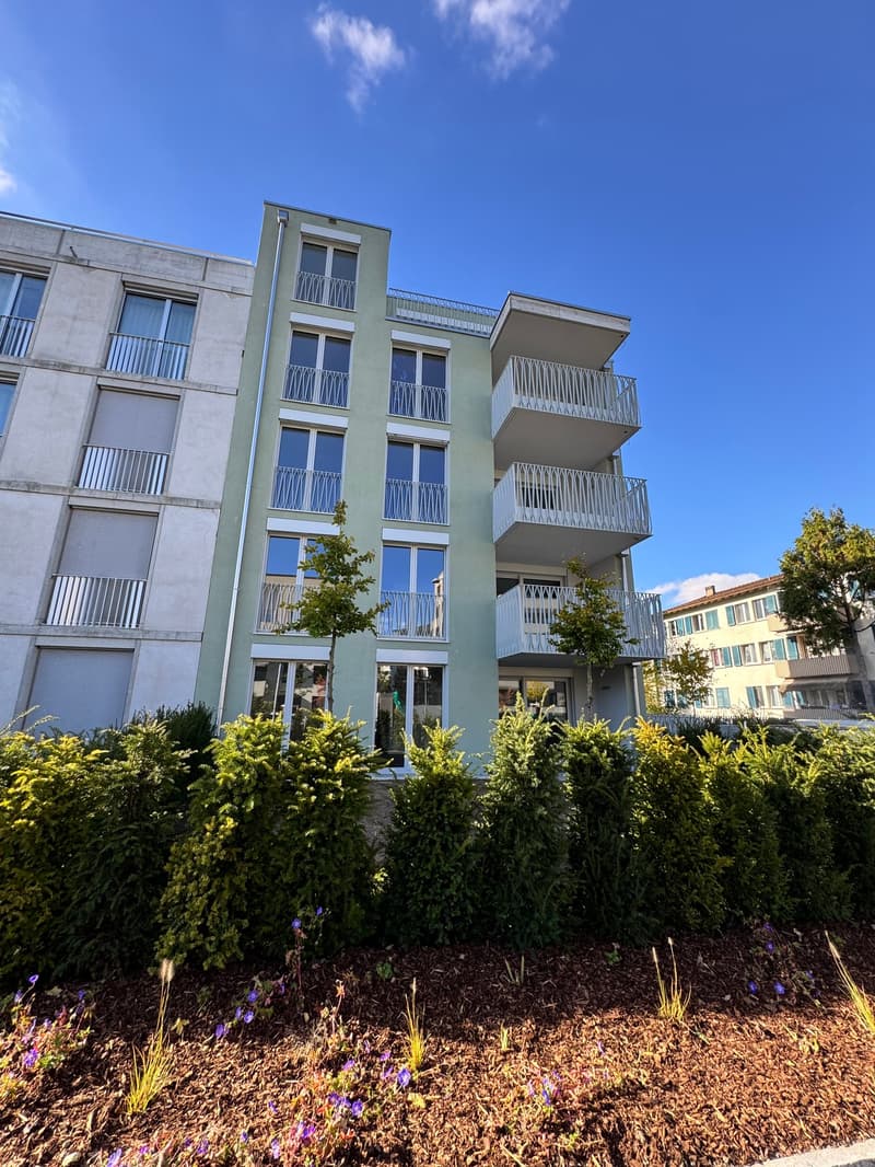 Modern apartment building with multiple balconies, glass windows, and a green facade