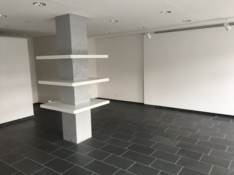 empty room, black floor tiles, white walls, three white shelves attached to central column, recessed lighting on ceiling